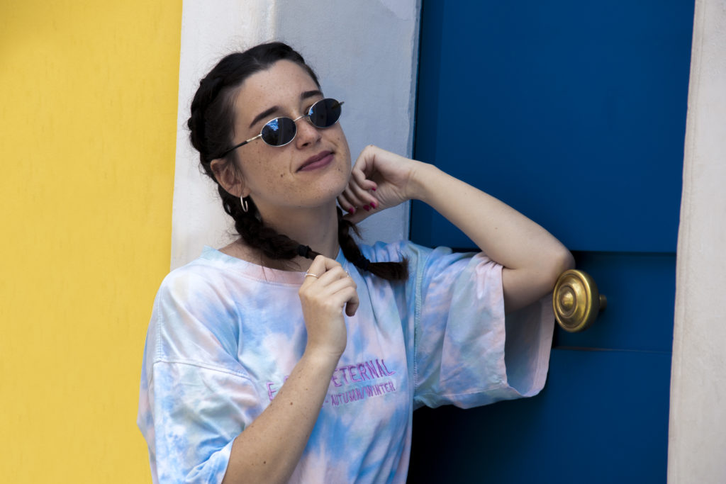 Femme brune avec lunette de soleil adossée à un mur